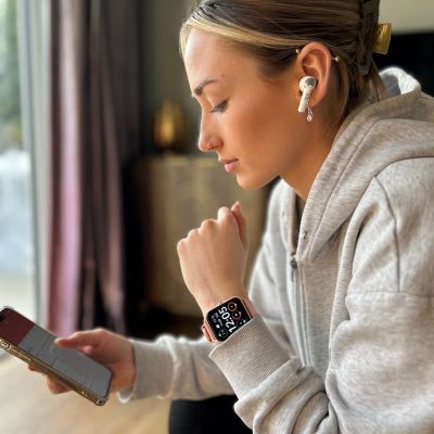 Woman using smartphone with smartwatch and earbuds in a home setting