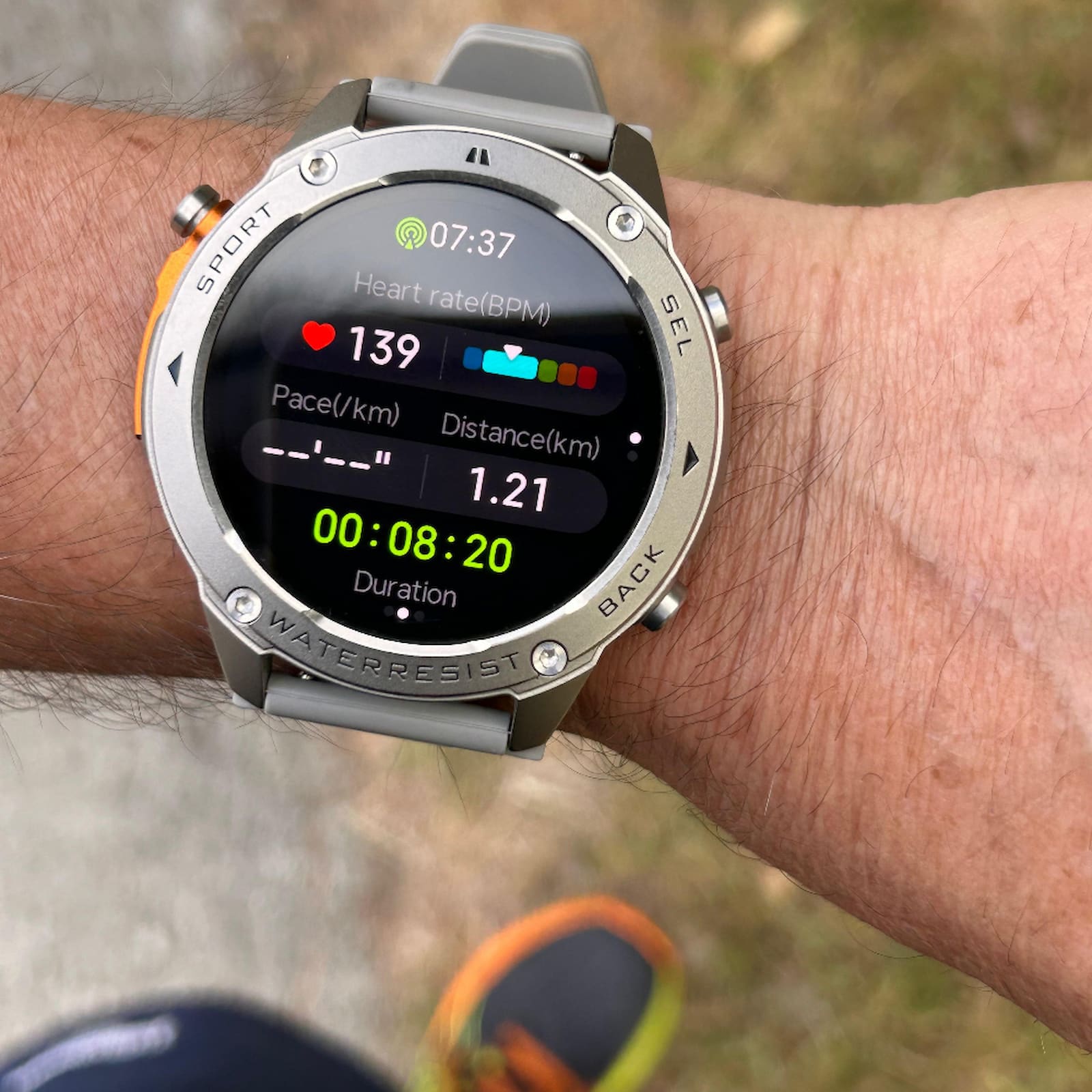 Smartwatch on a person's wrist displaying fitness metrics with a blurred outdoor background.