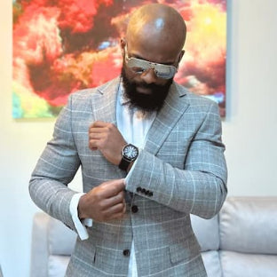 Man in a gray checkered suit adjusting his jacket in a room with colorful abstract art.